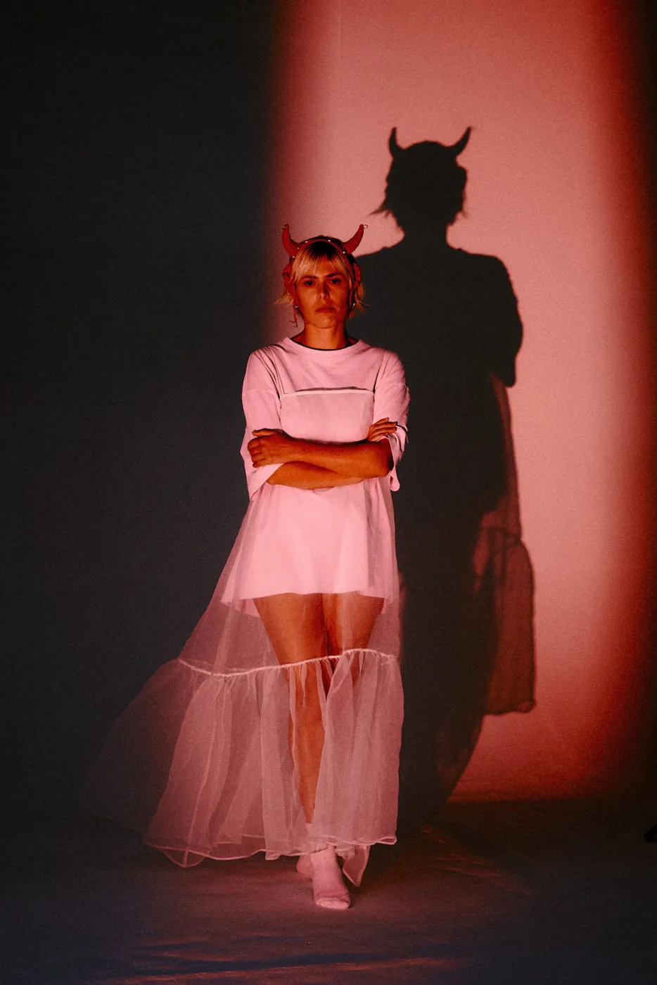 Ritratto in luce rosa di un'artista con corna rosse e abito di tulle